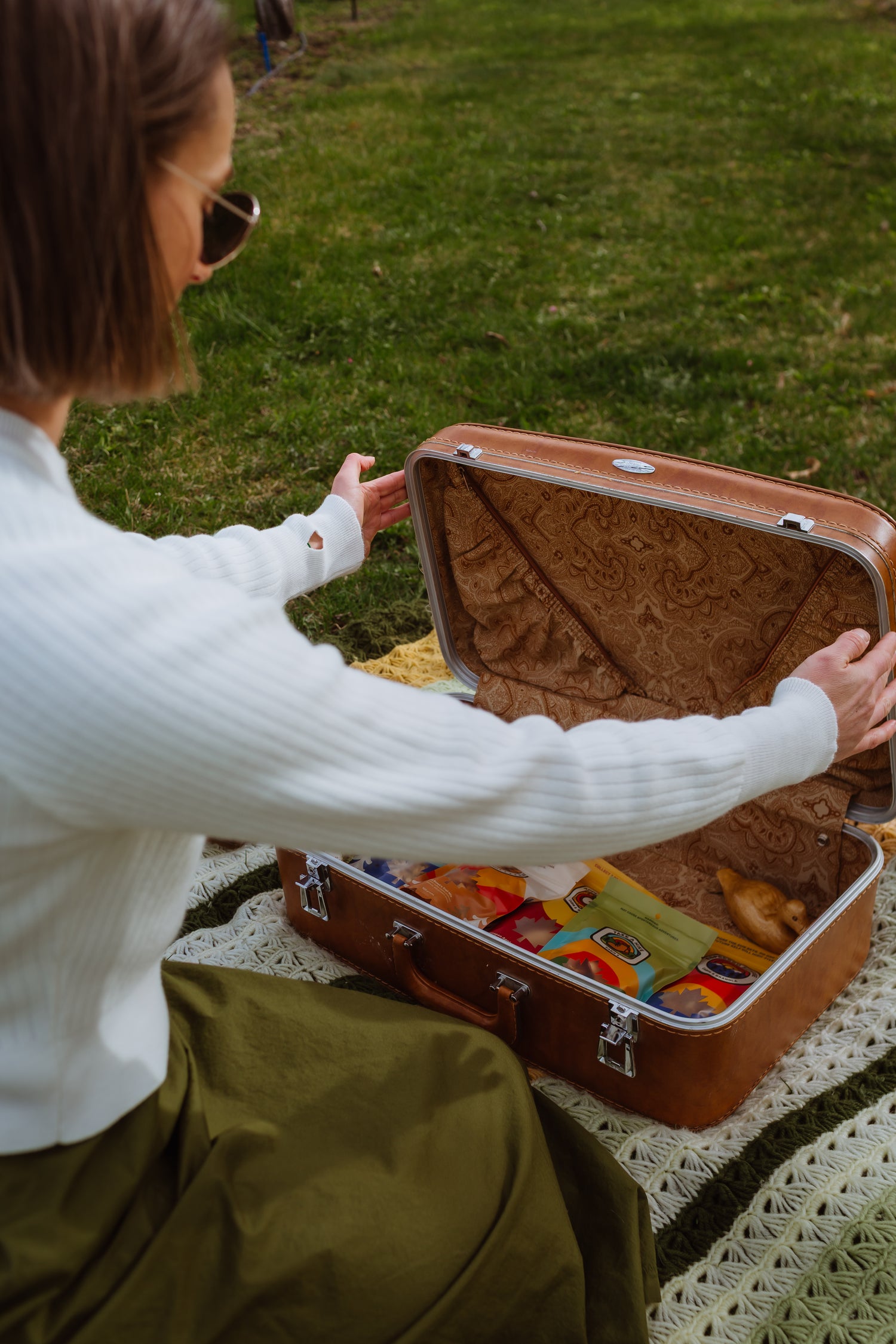 Person sitting on a blanket with an open suitcase filled with snacks outdoors